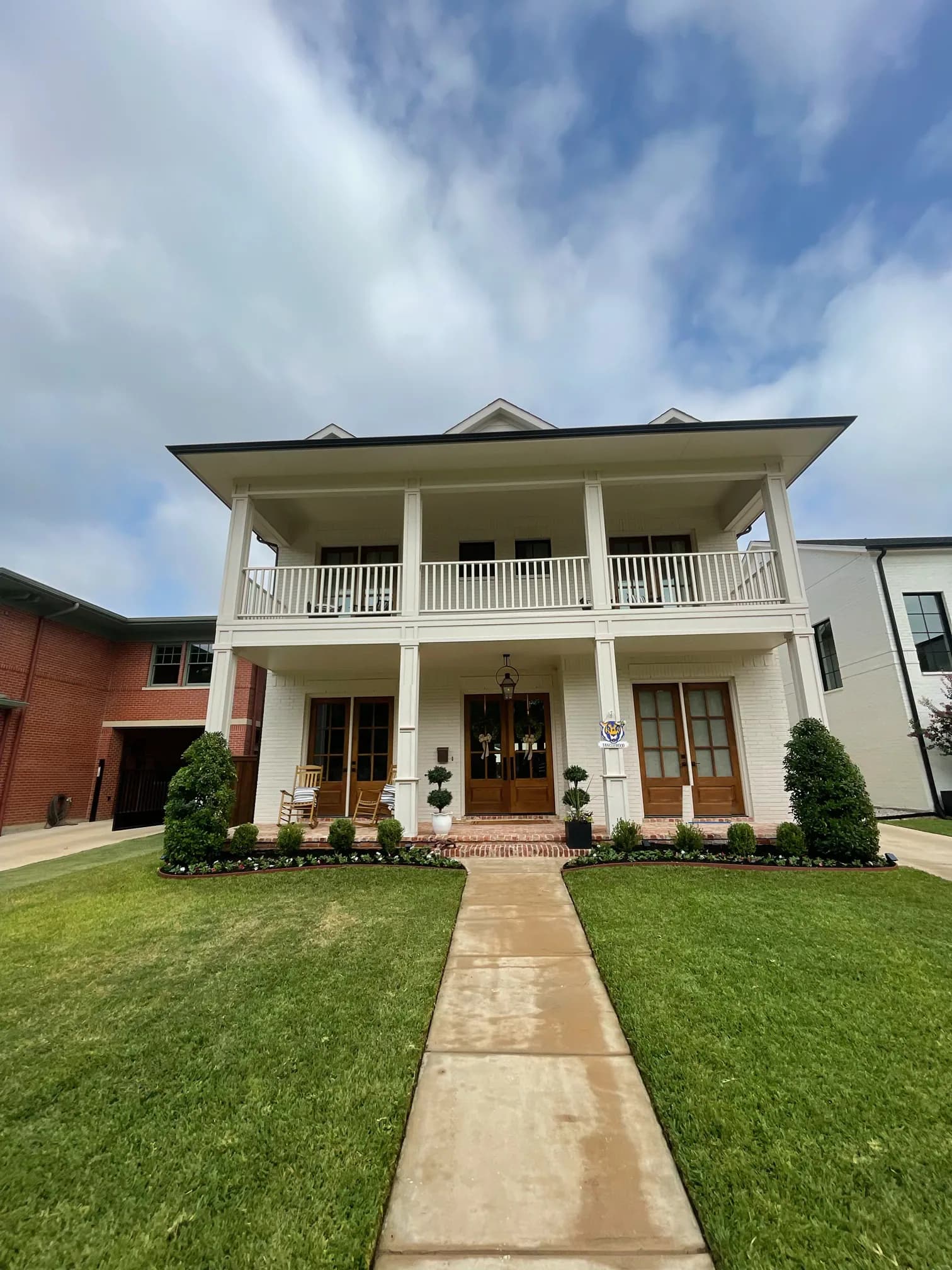 Front elevation of the two-story white brick house with double galleries, square columns, three sets of wood French doors and a straight walk through the lawn.