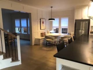 Looking across a black kitchen counter to a breakfast nook with a built-in bench, a round table and a black pendant, wainscoting on the walls.