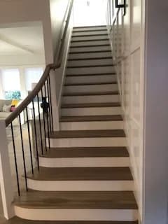 A straight run of wood stairs with white risers and a black metal balustrade.