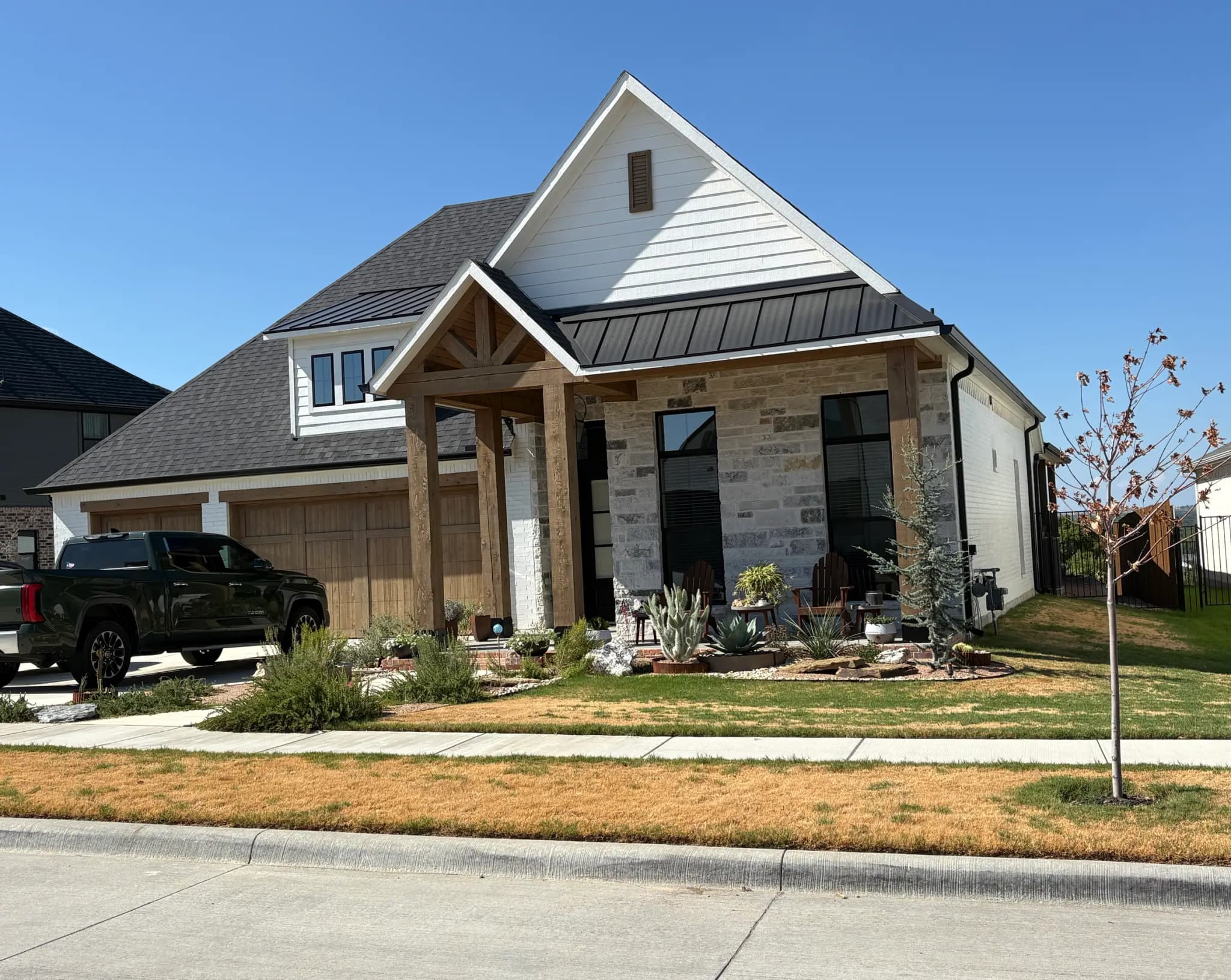 A modern farmhouse with a timber entry gable, a standing-seam metal accent roof, stone at the entry and a two-bay wood garage door.