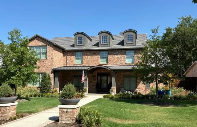 Wider view of the brick house: three arched dormers, the arched porch roof and the pillar planters at the street.