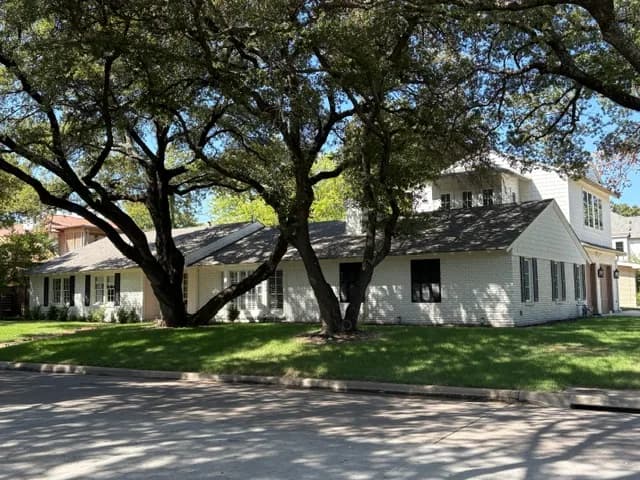 Wider street view of the white brick ranch and the second story under the trees.