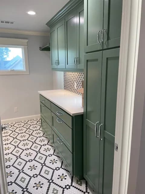 A laundry room in deep green cabinetry with a patterned tile backsplash and a hexagon mosaic floor.