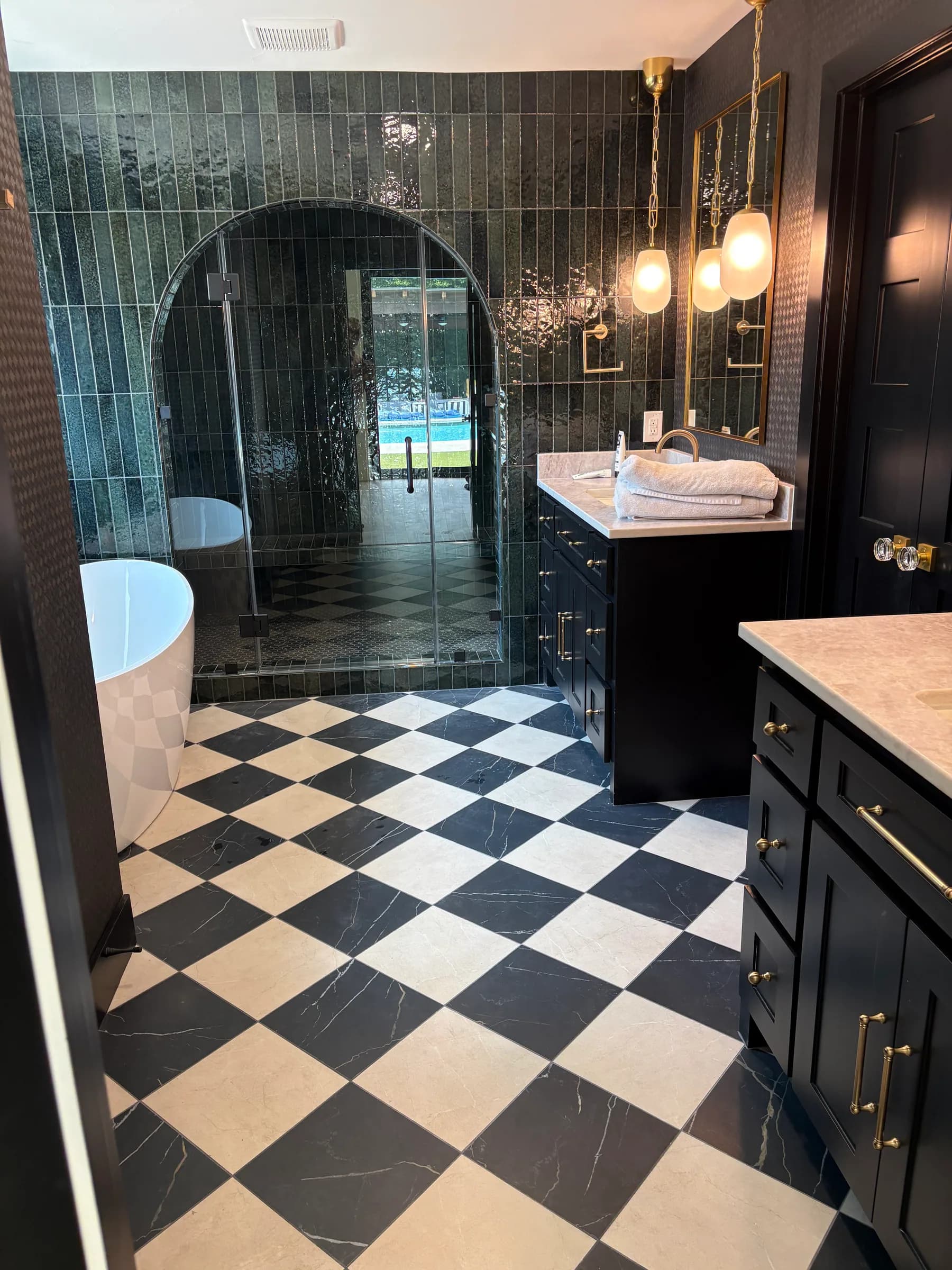 The black-tiled bathroom from the door: a freestanding tub, the arched shower, and the checkerboard floor.