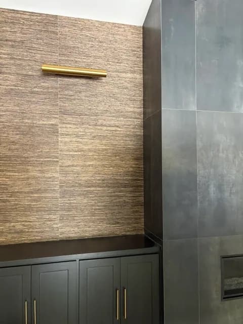 Woven-textured wallpaper with a brass picture light above black cabinets, beside a dark tiled fireplace wall.