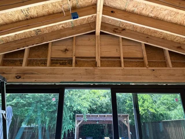 New roof framing over a wall of black-framed sliding doors, looking out to the pergola.