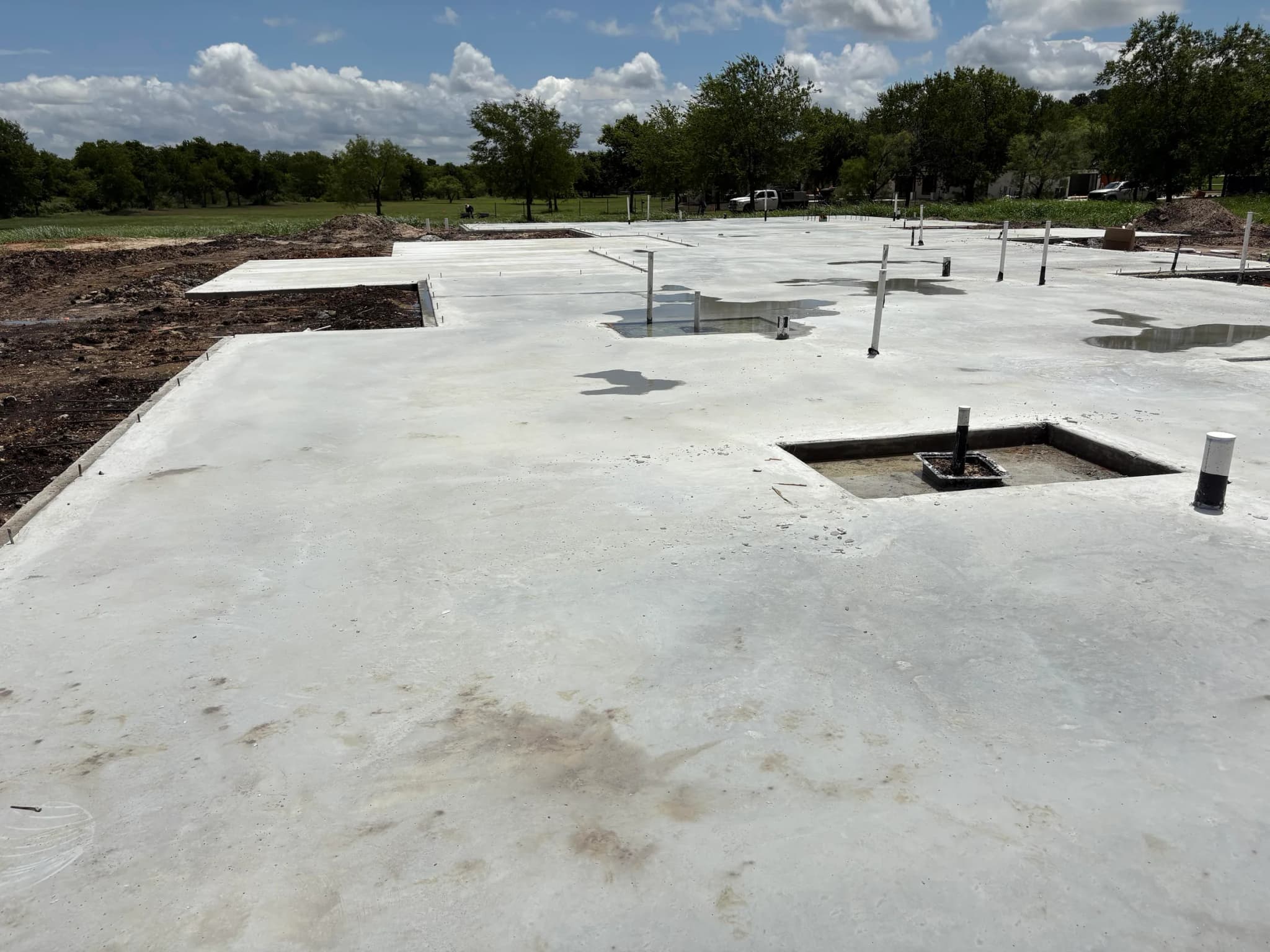 The poured slab from the far edge, block-outs and stub-ups across it and the excavated ground beyond.
