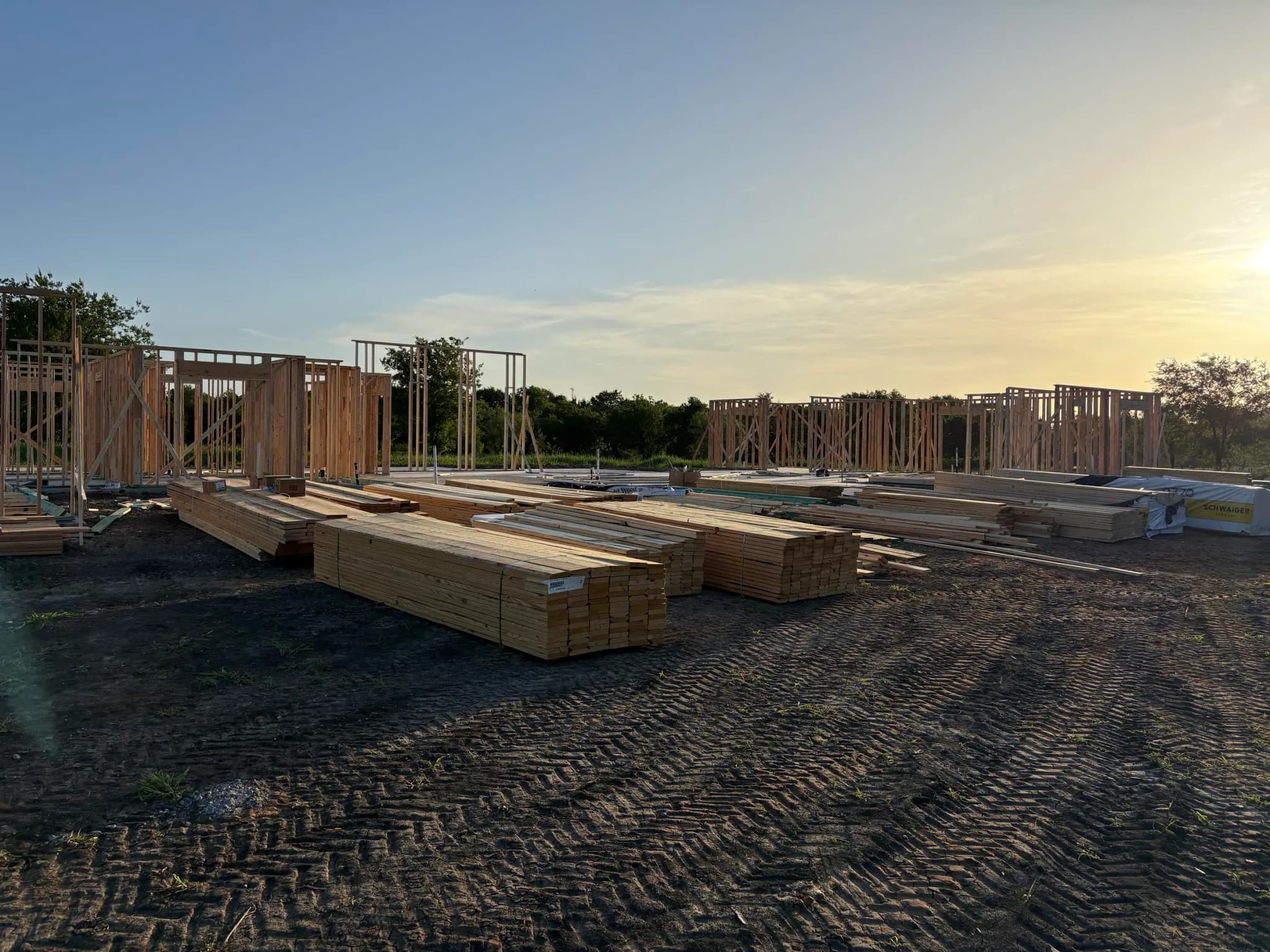 The standing stud walls in low sun, with lumber packs laid out across the graded ground.