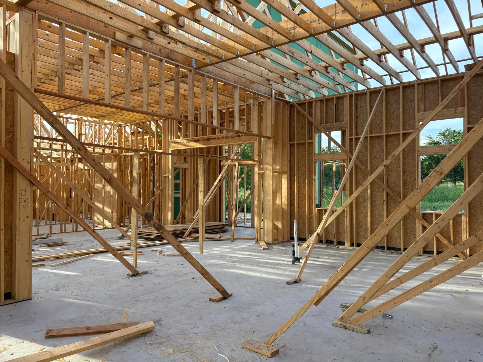 Interior framing looking through stud walls to open roof framing above, with temporary braces footed to the slab.