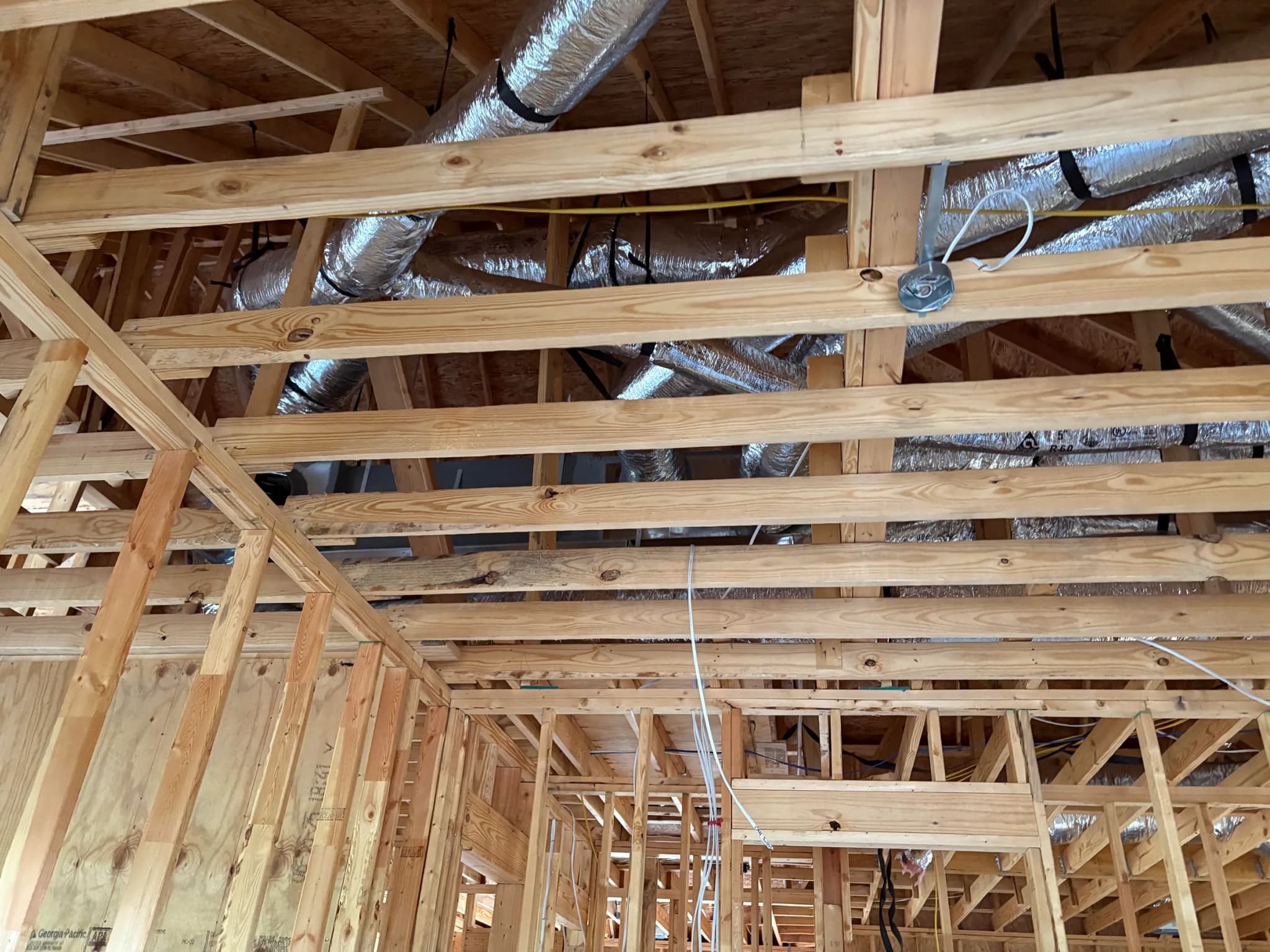 Roof framing from below with insulated flexible ducting run between the joists and electrical cable dropped to a ceiling box.