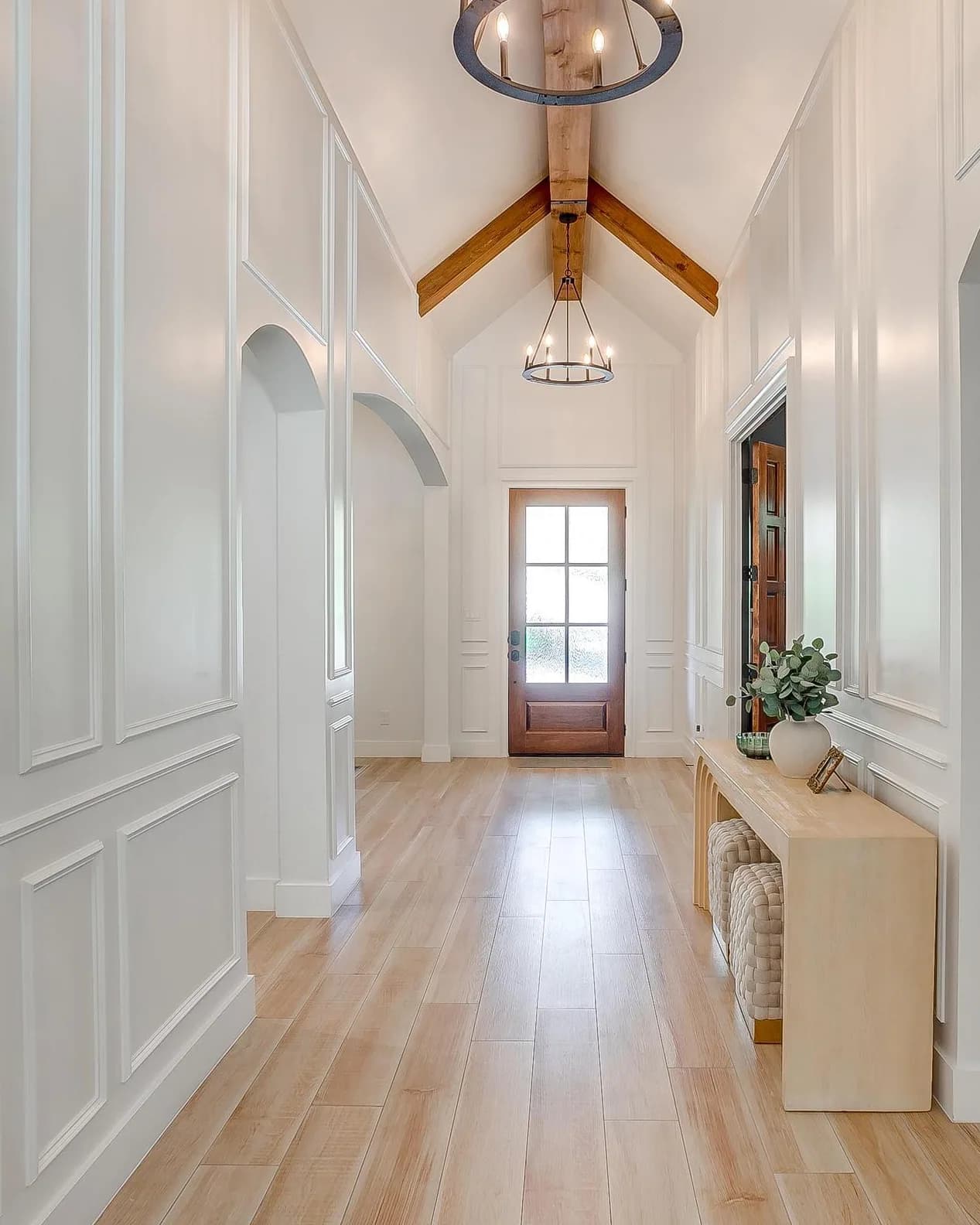 The entry hall: a vaulted ceiling with exposed wood ties, paneled white walls, arched openings to either side and a glass-paned door at the far end.