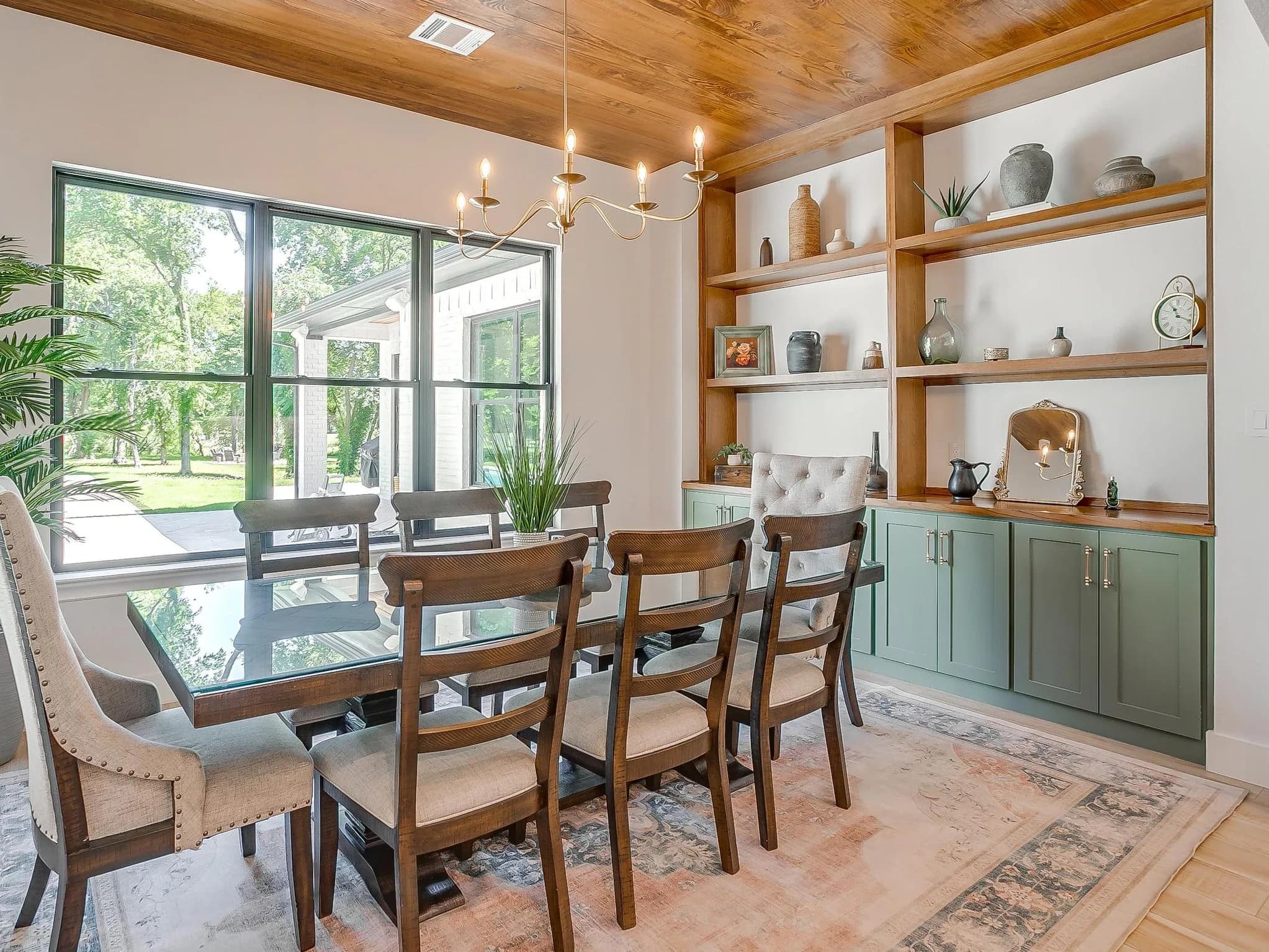 The breakfast room: a wood-planked ceiling, a window wall onto the patio, and built-in shelves over sage cabinets.
