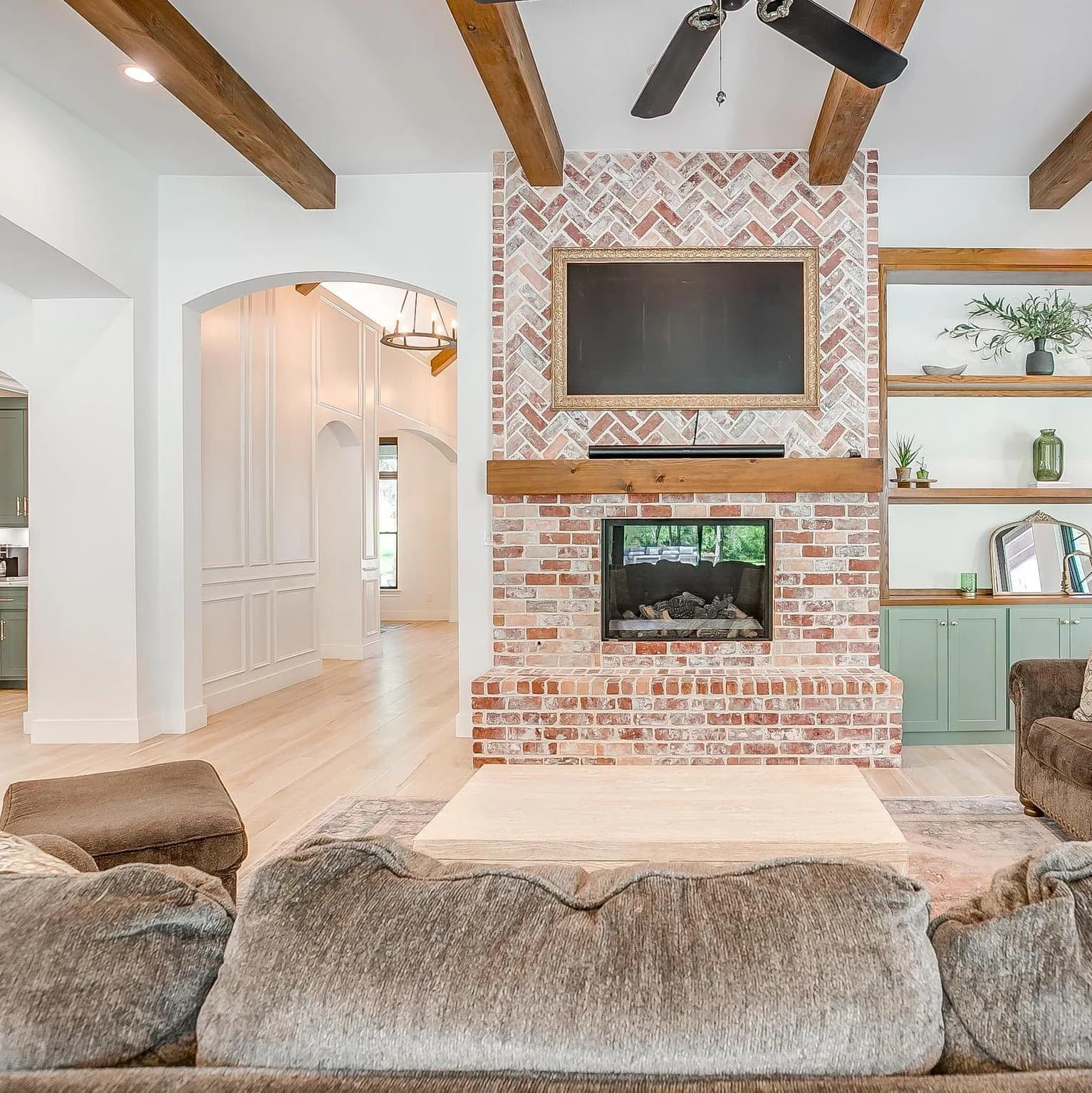 The fireplace head-on: red brick laid in herringbone at the firebox, a television above the mantel, and open wood shelves beside it.