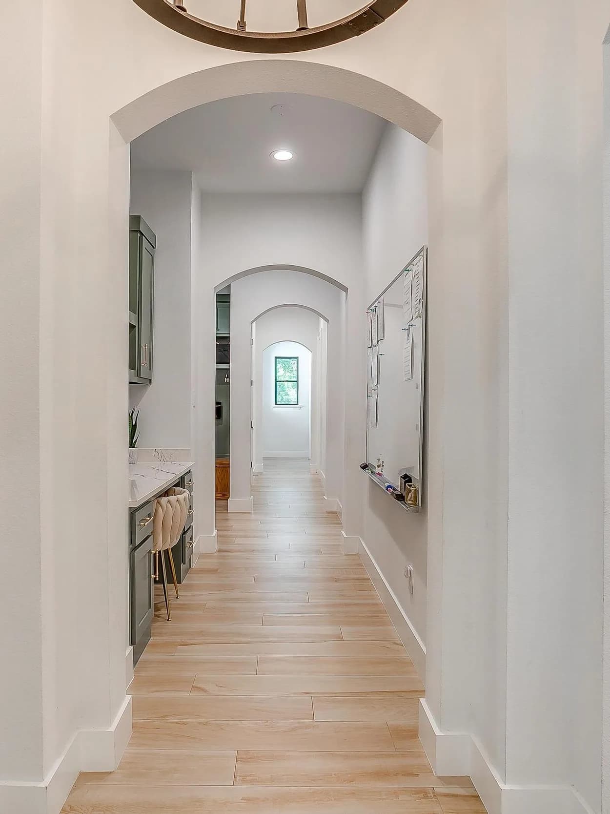 A long hall of white arches, one framing the next, with a glimpse of sage cabinets at the end.