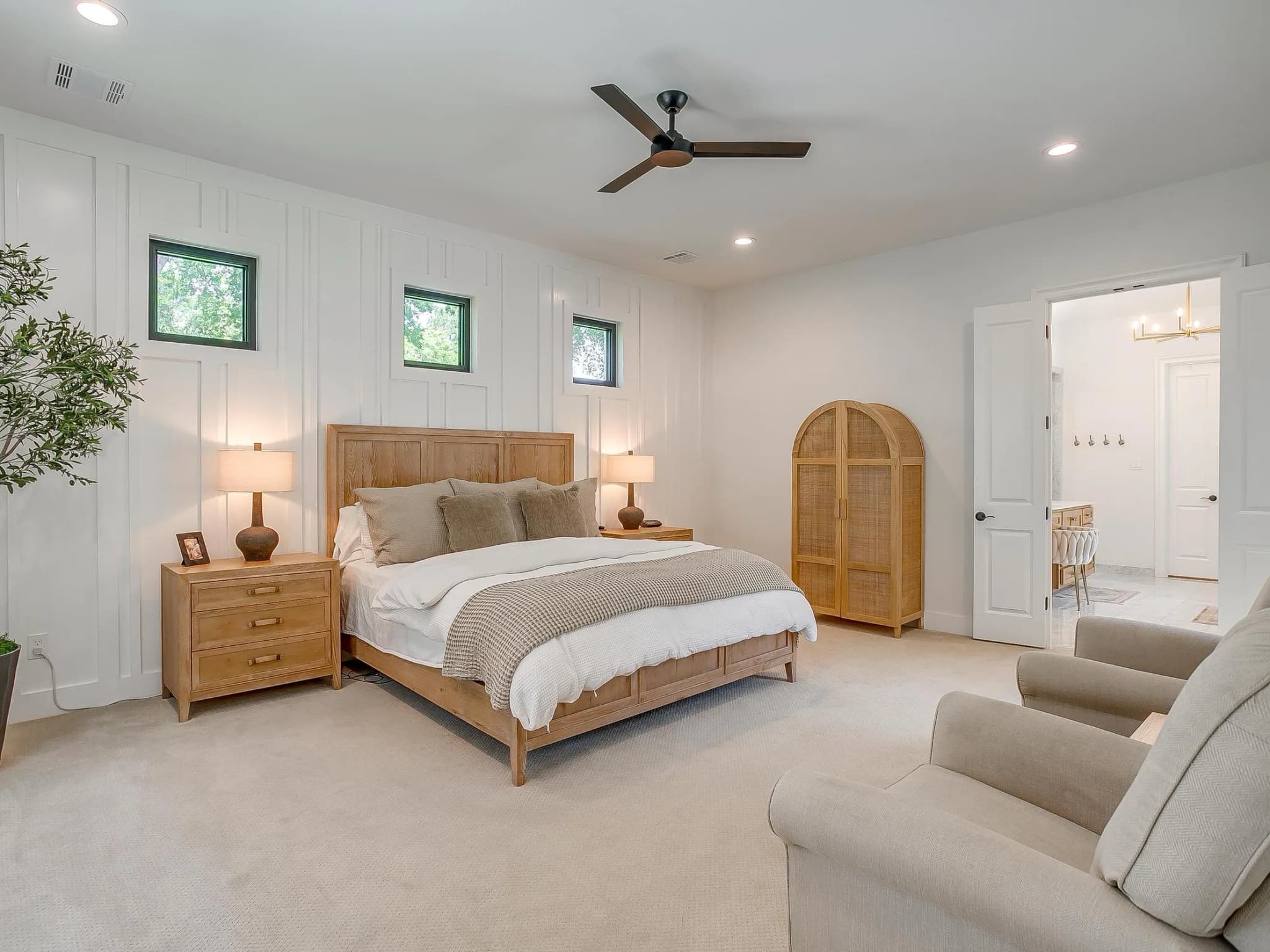 The primary bedroom: a tall vaulted ceiling with three small high windows over the bed, and arched wood cabinet doors to one side.
