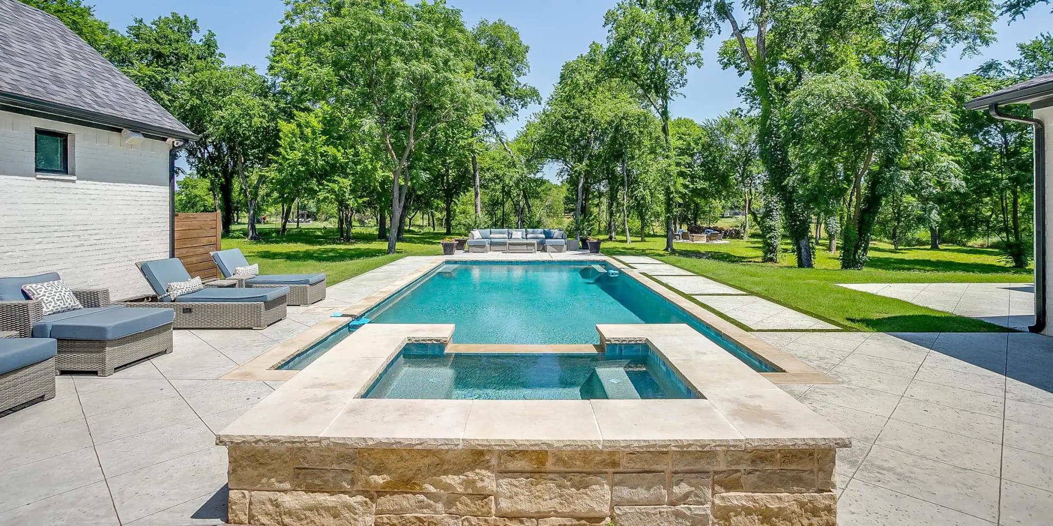 A raised spa with a stone surround spilling into the long pool, a shallow ledge and lounge chairs at the far end.