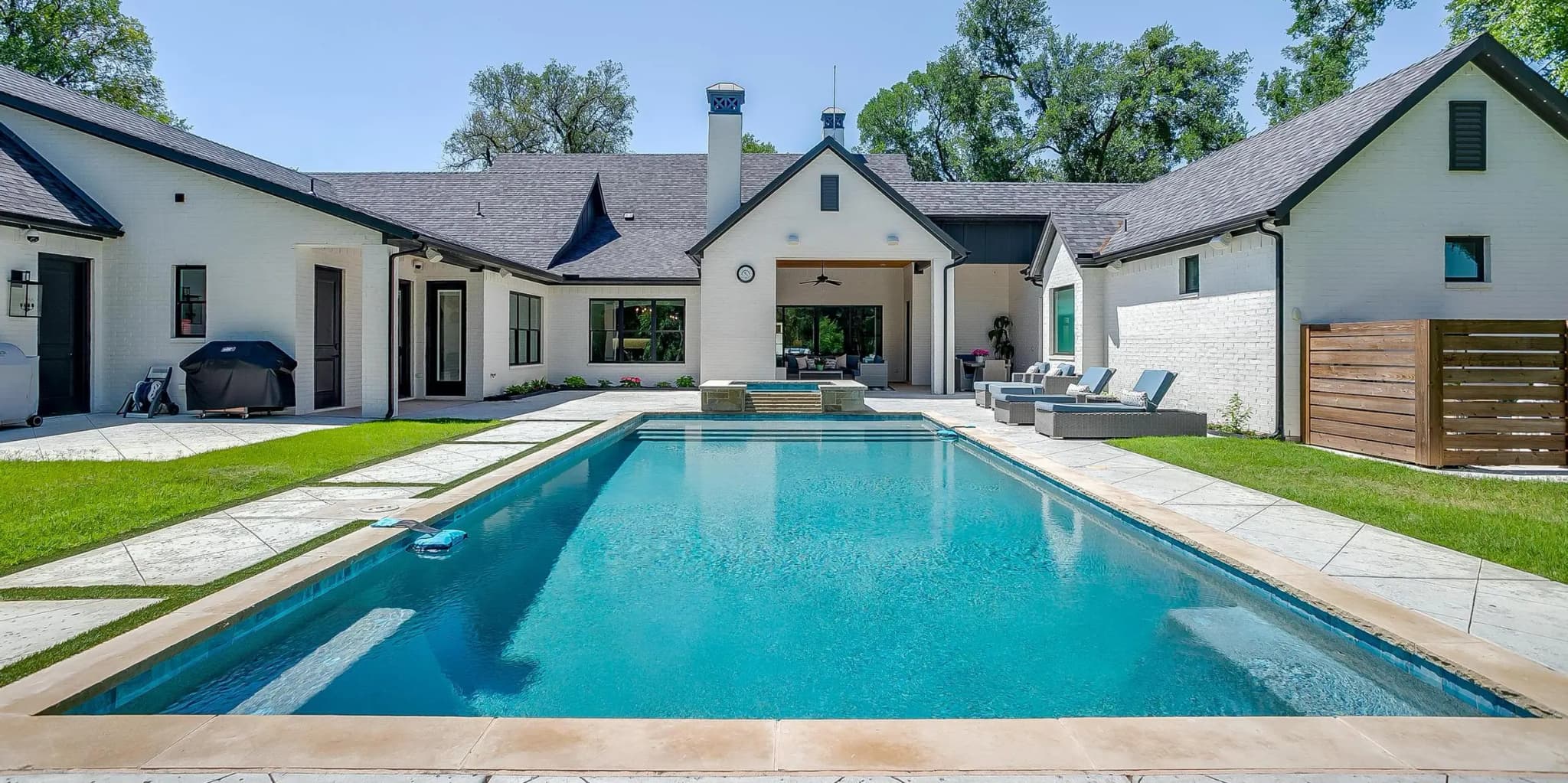 A long rectangular pool on axis with the covered patio, the white brick house spread wide behind it under dark roofs.