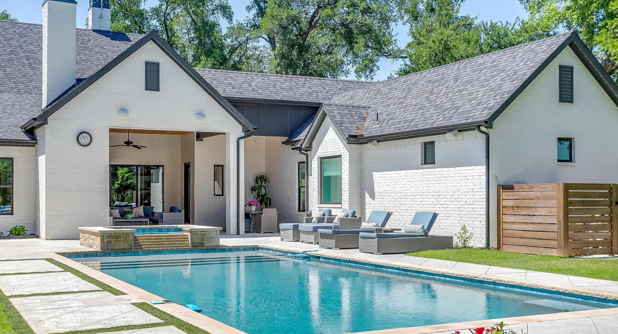 The corner of the house by the pool: white brick, a dark roof, the covered patio, and a slatted wood screen beside the spa.