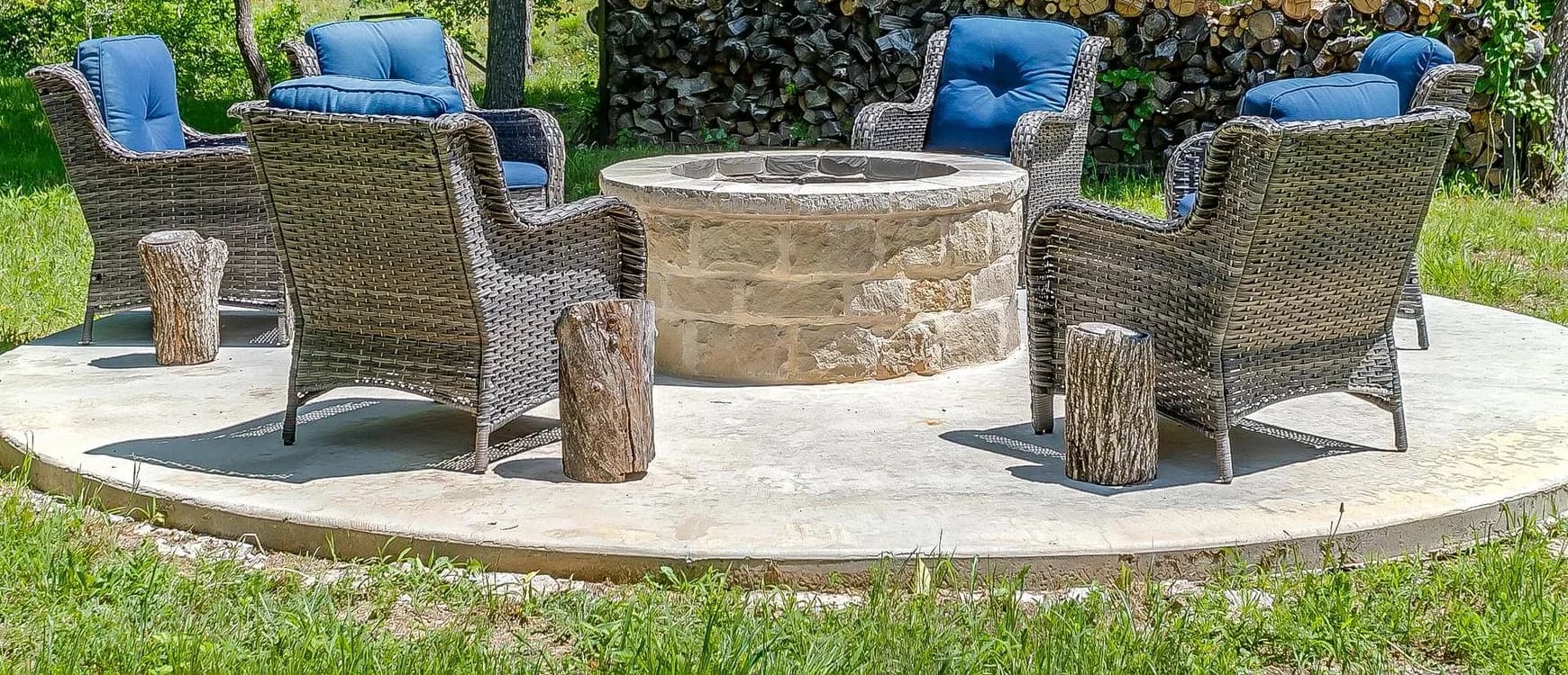 A round paved fire-pit circle with wicker chairs set among mature trees on the lawn.