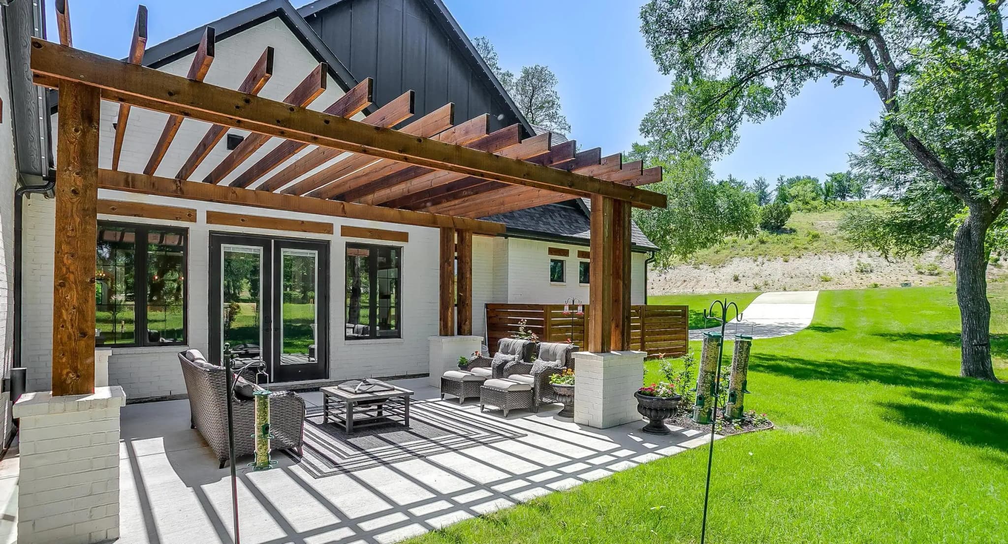 A second building with a dark gabled roof, a wood pergola over its patio and glass doors opening onto the lawn.