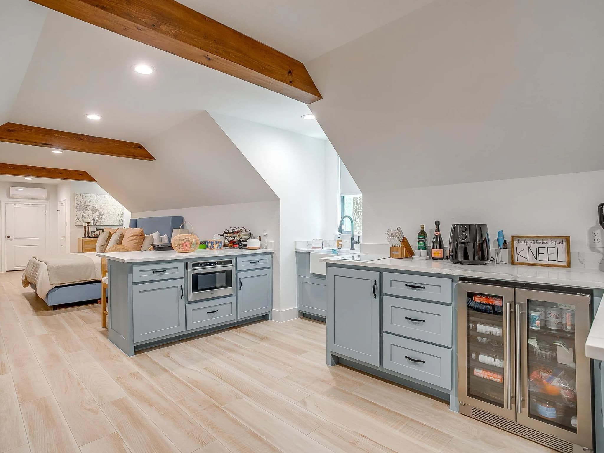 The room over the garage: a kitchenette in blue-gray cabinets under a sloped ceiling with exposed beams.