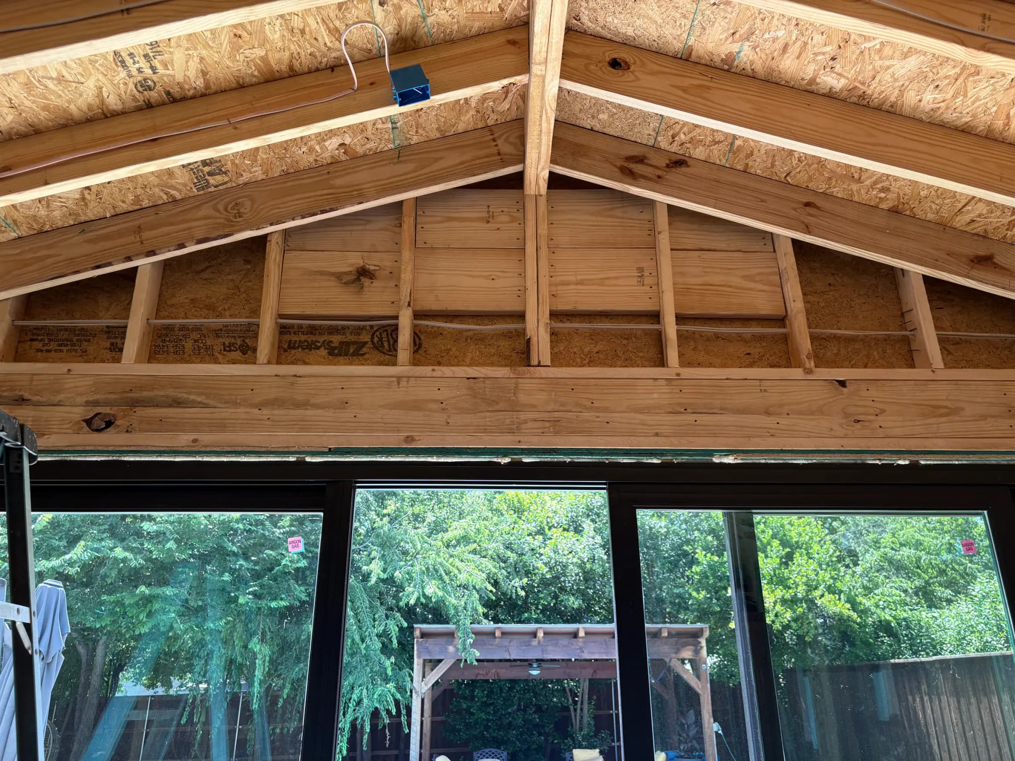 New roof framing over a wall of black-framed sliding doors, looking out to a pergola and a fence.