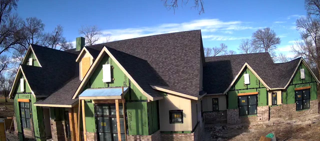 Brick laid along the base of one wing, the gables above it still sheathed.