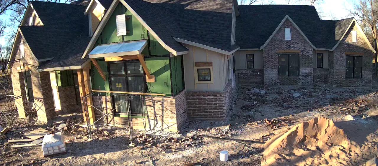 Brick across the wings and the chimney, the entry gable still sheathed behind its scaffolding.
